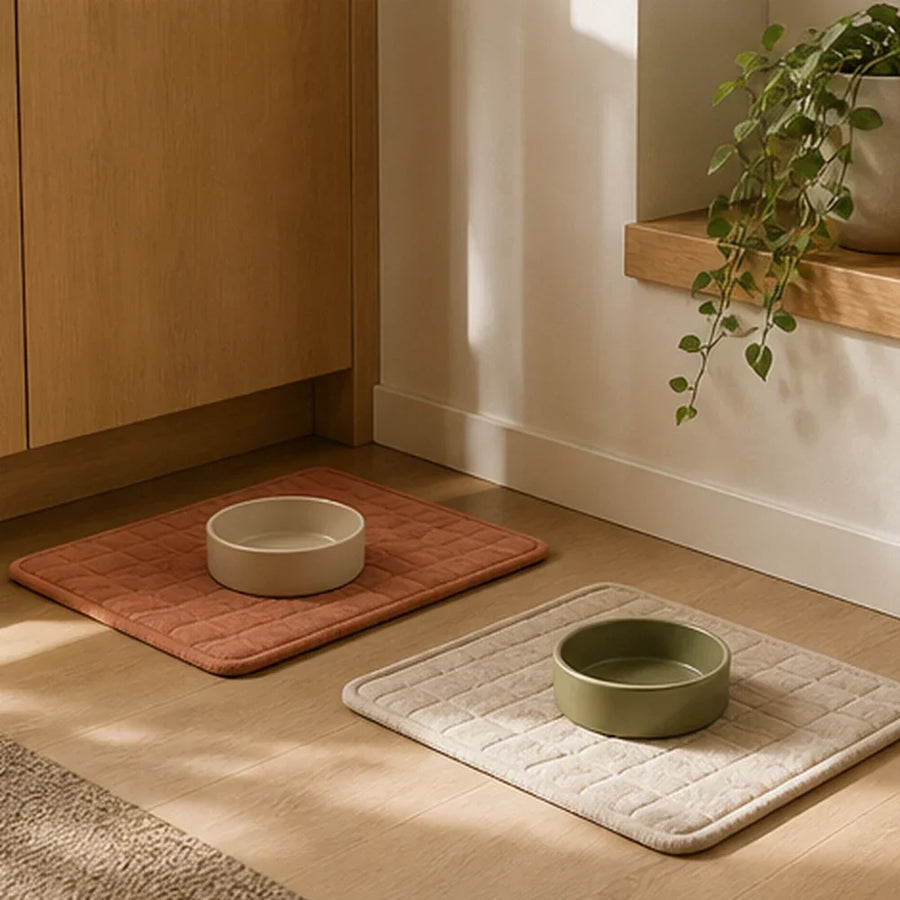 A dog bowl and cat bowl placed on two washable mats in a warm kitchen corner